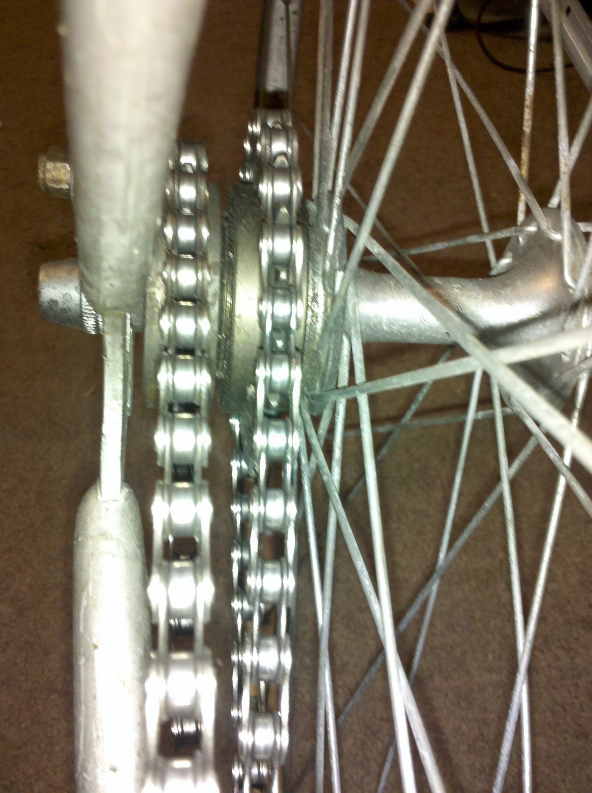 Photo of a bicycle; looking from the seat tube back toward the rear wheel. From right to left there is the stays and dropout, a chain running over a smaller single-speed freewheel, a chain running over a larger single-speed freewheel, and the hub and spokes. 