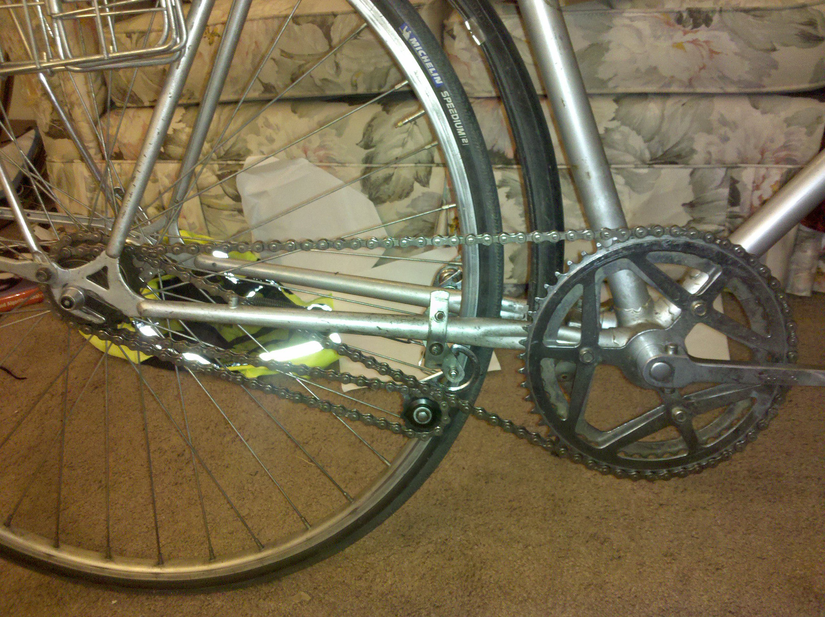 Photo of a bicycle drivetrain. The chainline is unusual. Chain runs from the top of the front chainring back over a small single-speed freewheel on the rear hub, then forward to a tensioner pulley mounted behind and below the chainring. The chain wraps around the tensioner and turns back to the rear hub, where it goes around a larger single-speed freewheel and runs from the top of that freewheel to the bottom of the front chainring. It wraps around the chainring, and we're back at the start. 

The tensioner pulley is made from pieces of an old rear derailer.